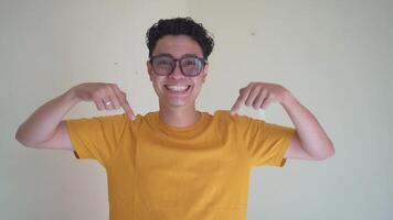 Young Indonesian curly man wear yellow t-shirt with press link thumbnail gesture.  The footage is suitable to use for man expression and people advertising content media. video