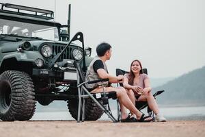 joven Pareja se involucra en un animado charla mientras sentado por su fuera del camino coche a un pacífico orilla del lago cámping lugar. foto