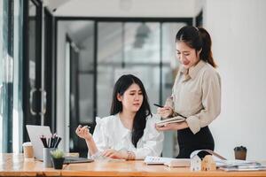 Two engaged female colleagues review notes and discuss project details, with one taking the lead in explaining, highlighting the synergy in a professional team environment. photo