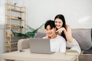 Cheerful couple is engaged in an entertaining activity on a laptop in a well-lit and tastefully decorated living room. photo