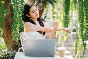 A relaxed woman stretches her arms taking a break from work on her laptop in a serene garden setting. photo