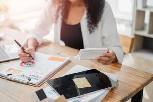 Focused businesswoman using a calculator and reviewing financial reports, surrounded by various work documents on her desk. photo