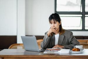 Businesswoman looks on with concern while working on her laptop, reflecting on a serious matter or decision in a cafe setting. photo