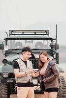 Young couple stands together outdoors, sharing a moment over a vintage camera with a car in the background. photo