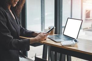 Close-up back view of a business woman working in the office using smartphone and laptop with blank screen, looking at the screen. photo