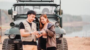 Young couple stands together outdoors, sharing a moment over a vintage camera with a car in the background. photo