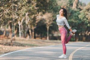 Fitness concept, Fit young female runner stretching her leg during a warm-up in a sunny park pathway. photo