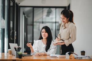 Two professional women engaging in a collaborative work discussion with laptops and notes on a bright office desk. photo