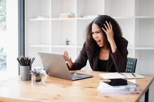 estresado y frustrado mujer de negocios reacciona a contenido en su ordenador portátil pantalla, un momento de desafío o inesperado problema a trabajar. foto