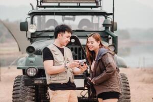 Young couple stands together outdoors, sharing a moment over a vintage camera with a car in the background. photo