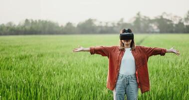 Young woman stands with arms wide open, wearing a VR headset in a lush green field, embracing the virtual experience. photo