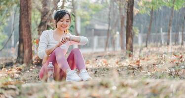 Smiling woman in sportswear checking her fitness tracker after exercising, seated in a serene forest area. photo