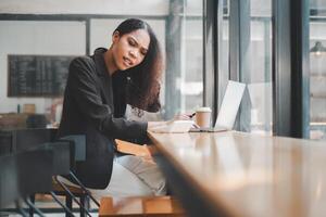 un joven mujer de negocios experiencias incomodidad mientras trabajando a su ordenador portátil en un café comercio, reflejando el retos de remoto trabajar. foto