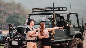 Man and woman engage in exploration, the woman pointing into the distance, with a vintage off road car in the foreground. photo