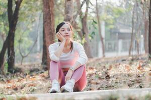 Thoughtful woman takes a break from her workout to sit and reflect on a sun-dappled path in a tranquil forest. photo