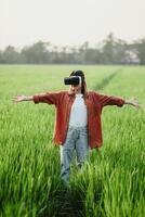 Woman spreads her arms wide while immersed in a virtual reality experience in a lush field of tall grass. photo