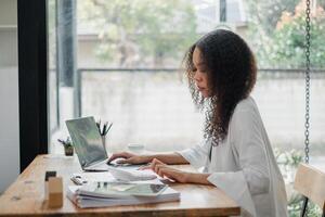 Diligent professional with curly hair is fully absorbed in her work, typing on a laptop in a bright room bathed in natural light. photo