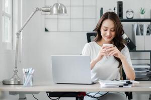 Relaxed professional woman savoring a coffee break at her home office, with a gentle smile and a casual posture, enjoying her workday. photo