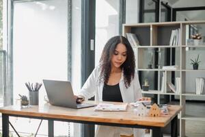 Real estate agent attentively examines property listings on her laptop in a stylishly furnished office, symbolizing professionalism and dedication. photo