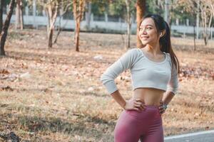 A fit young woman pauses to rest, hands on hips, after a run in a peaceful park setting, embodying a commitment to health and fitness. photo