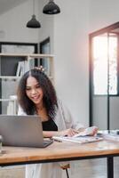 Bright and cheerful businesswoman sorting through paperwork with a laptop open in a modern, naturally lit office space. photo