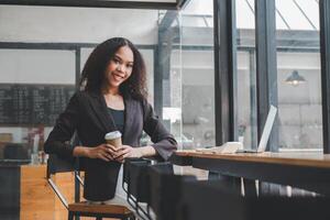 Confident young businesswoman at a cafe with laptop and hand holding coffee mug, ready for a productive workday. photo