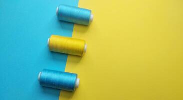 carretes de hilo y un aguja en un amarillo y azul fondo, contraste concepto foto