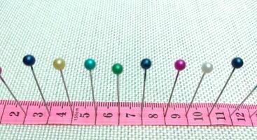 sewing needles and pins of different colors, ruler on white cloth background photo