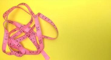 pink measuring tape on a yellow background. Rolled tape with numbers photo