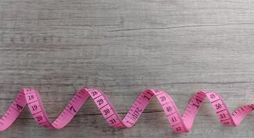 pink measuring tape on a wood background. Rolled tape with numbers photo