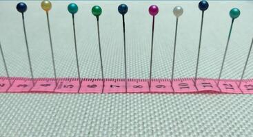 sewing needles and pins of different colors, ruler on white cloth background photo