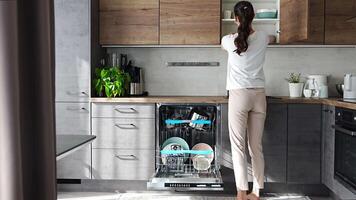 een vrouw verwijdert schoon keramisch gerechten van afwasmachine. huishouden en nuttig technologie concept. hoog kwaliteit 4k beeldmateriaal video