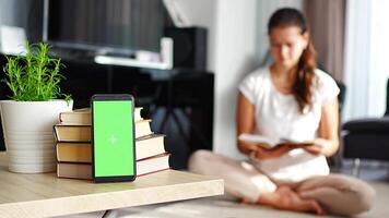 Digital detox concept photo. Smartphone with green chroma key screen and woman reading book in the background. High quality 4k footage video