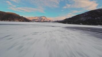 velozes fpv zangão voar sobre uma congeladas lago com coberto de neve pôr do sol montanhas dentro a fundo video