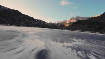 The surface of the frozen water of a lake in winter from a height, overflying on a sports FPV drone. There is a snow-capped mountain in the background. Tourists go ice skating here this season video