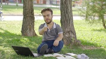 college dwerg leerling pratend terwijl op zoek Bij camera terwijl aan het studeren in de park. video