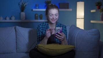 Woman using social media on phone laughing at night at home. video