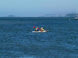 Berkeley, CA, 2008 - two-man kayak on bay with moored sailboat photo