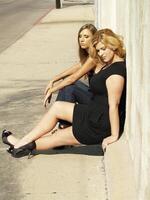 Two Women Sitting Curb Sidewalk Sunny Day photo