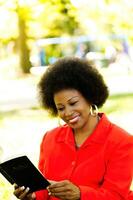 de edad mediana africano americano mujer sentado leyendo Biblia en parque foto