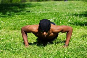 joven africano americano hombre haciendo Lagartijas a parque en césped foto