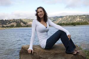 Young caucasian woman sitting on rock at lake photo