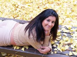 joven Hispano adolescente niña en banco con otoño hojas foto