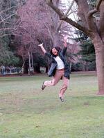 Young hispanic teen girl jumping in park photo