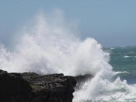 Ocean Wave Crashing Into Rock Shore With Blue Sky photo