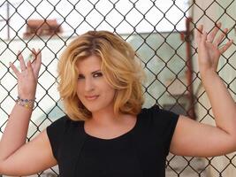 Plump blond woman against chain linked fence photo