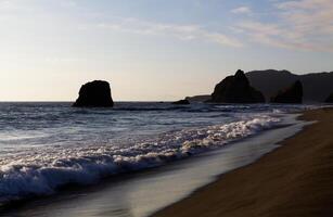 Oceano olas en arena playa con apagado apuntalar rocas foto