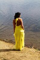 mujer en pie en río banco mirando a agua en amarillo vestir foto