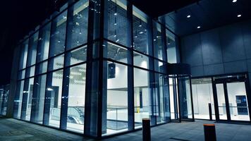 Night view on the ground floor of modern office building with big glass windows and entrance. Street reflection. photo