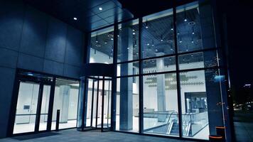 Night view on the ground floor of modern office building with big glass windows and entrance. Street reflection. photo